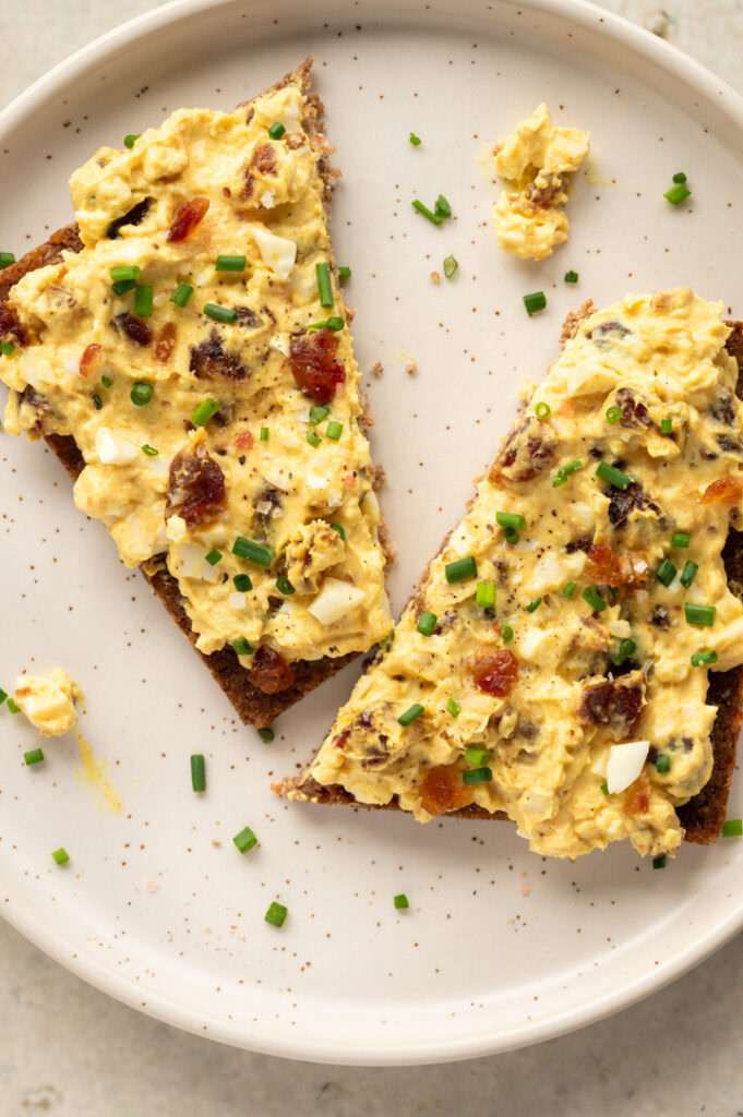 Ein angeschnittenes Roggenbrot mit Eiersalat mit Curry und Datteln liegt auf einem Teller.