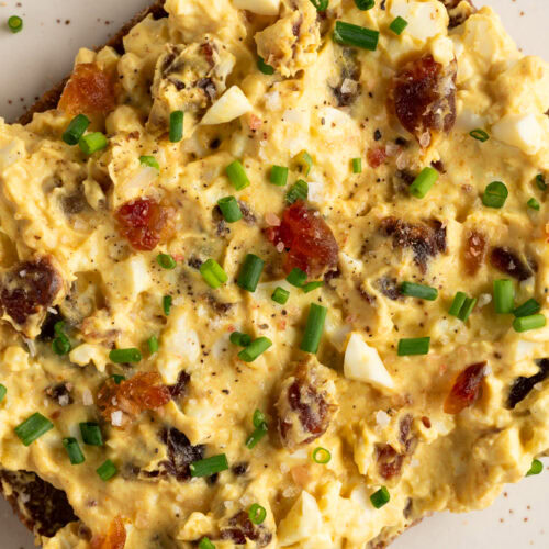 Eine Scheibe Roggenbrot bestrichen mit Eiersalat mit Curry und Datteln liegt auf einem Teller.
