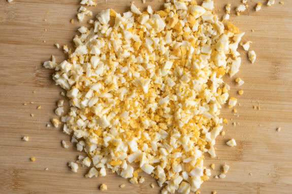 Klein geschnittene Eier liegen auf einem Brett.