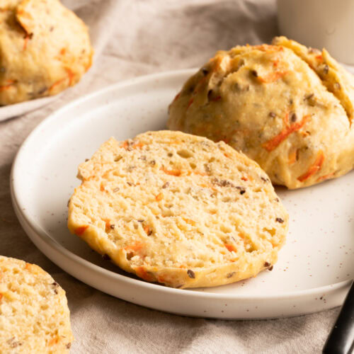 Ein Teller mit einem aufgeschnittenen Karottenbrötchen steht auf einem Tisch.