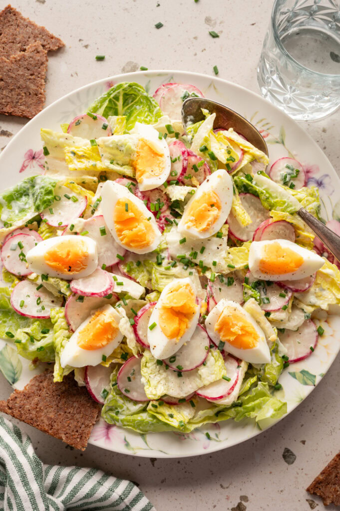 Ein Teller mit Radieschensalat mit Ei und Joghurtdressing steht auf einem Tisch.