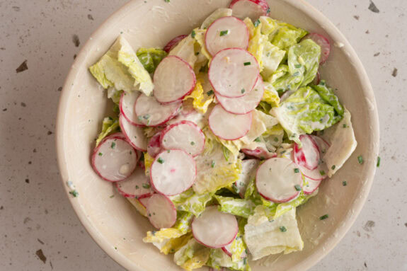 Eine Schüssel mit Salat, Radieschen und Dressing.