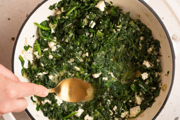 Eine Person drückt mit einem Löffel Mulden in den Spinat.