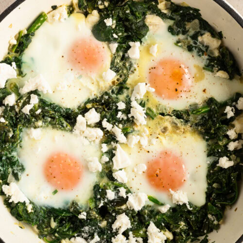 Eine tiefe Pfanne mit Spinat und Eiern steht auf dem Tisch.