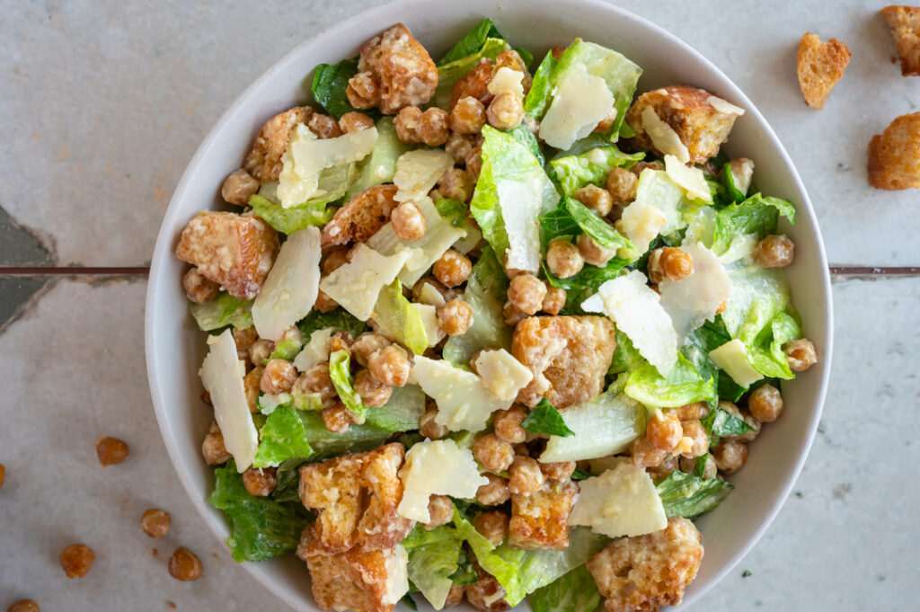 Eine Schüssel mit vegetarischem Caesar Salat mit Kichererbsen steht auf dem Tisch.