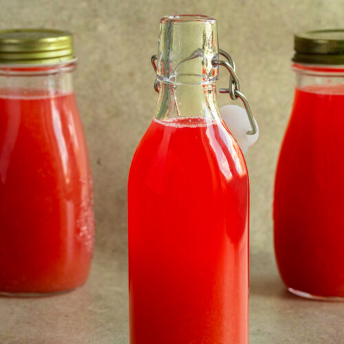 Drei Flaschen mit selbst gemachtem Rhabarbersirup stehen auf einem Tisch.