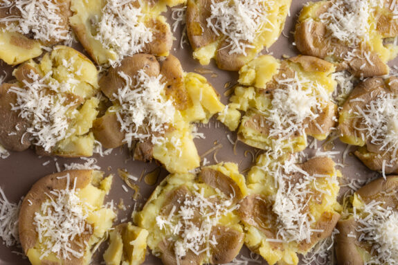 Parmesan und Olivenöl werden auf den Kartoffeln verteilt.
