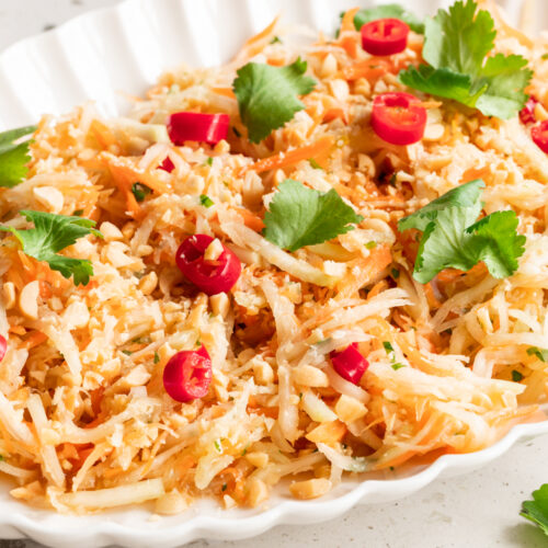 Eine Servierschale mit asiatischem Kohlrabisalat steht auf dem Tisch.
