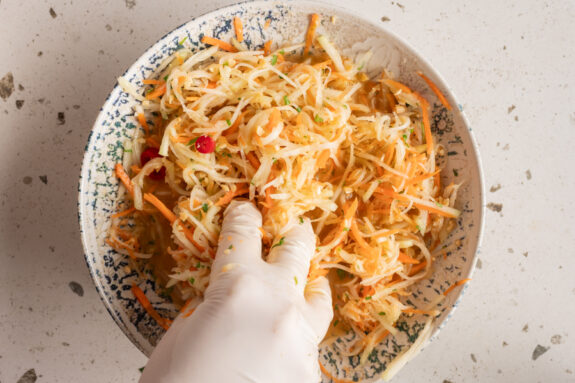 Eine Person knetet den Salat mit den Händen.