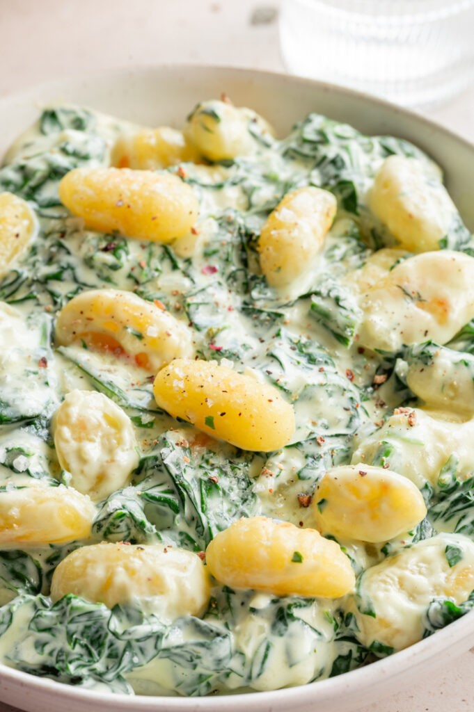 Ein Teller mit Gnocchi mit Spinat stehen auf dem Tisch.