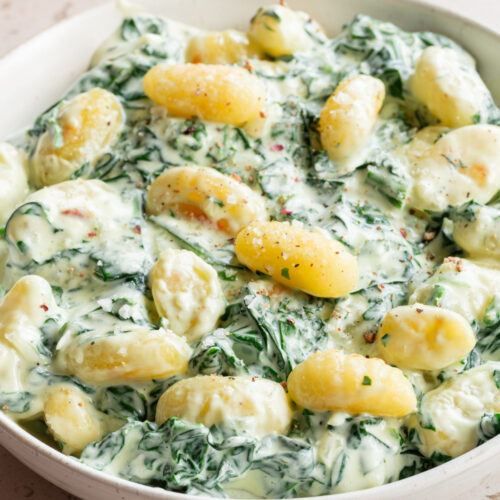 Ein tiefer Teller mit Gnocchi mit Spinat in Sahnesauce steht auf dem Tisch.