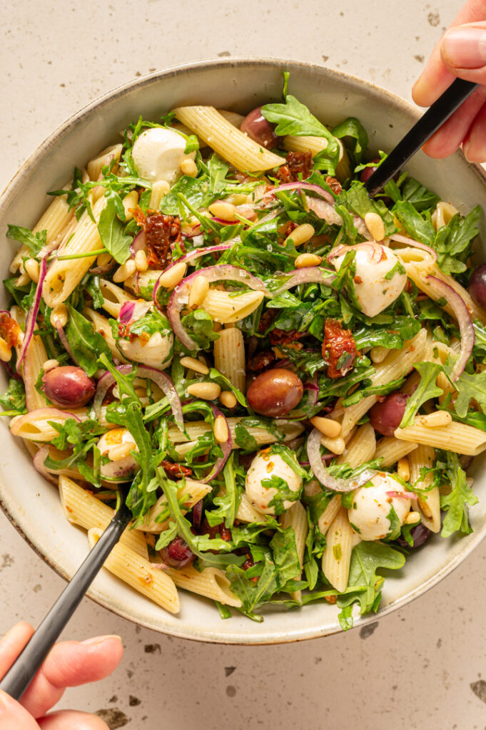 Eine Person verrührt den italienischen Nudelsalat mit Salatbesteck.