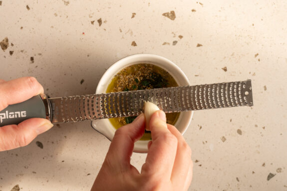 Eine Person gibt den Knoblauch zu den anderen Zutaten für das Dressing.