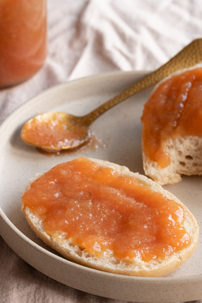 Ein Teller mit einem Brötchen belegt mit Rhabarber Marmelade steht auf einem Tisch.