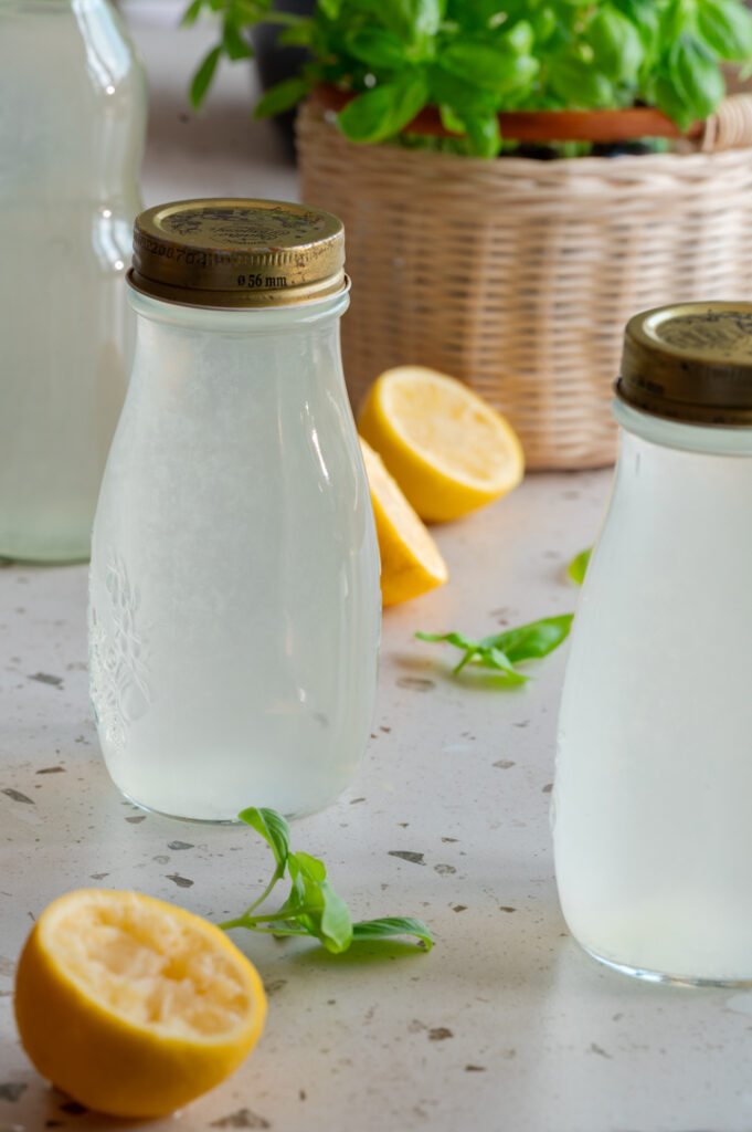 Drei Flaschen mit selbst gemachtem Sirup mit Basilikum und Zitrone stehen auf dem Tisch.