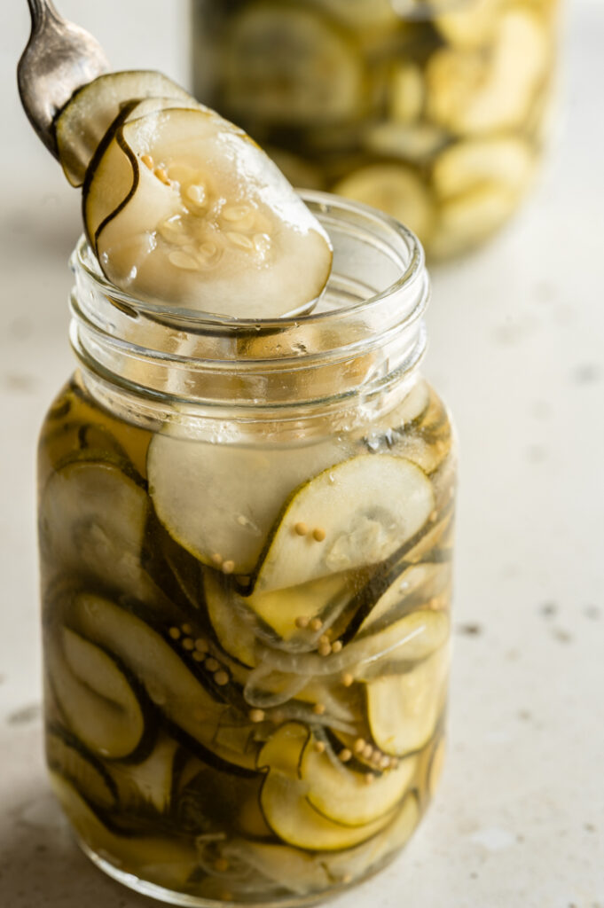 Eine Person nimmt eingelegte Zucchini mit einer Gabel aus dem Glas.