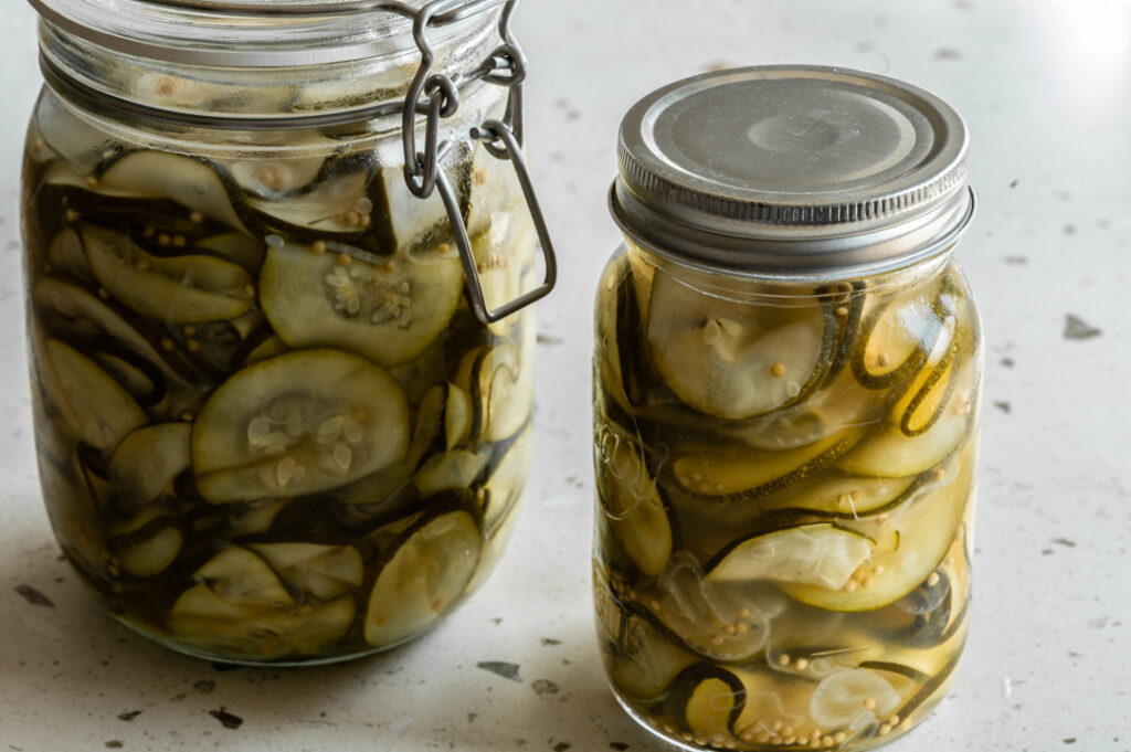 Zwei Gläser mit eingelegter Zucchini stehen auf dem Tisch.