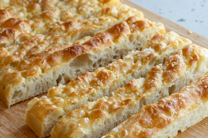 Eine Focaccia ohne Kneten liegt auf einem Brett.