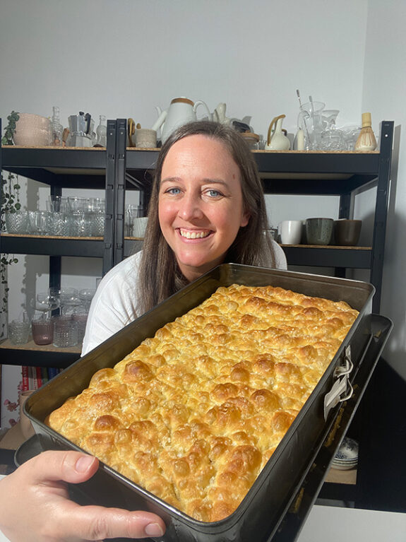 Eine Person hält die eckige Springform mit Focaccia in der Hand.