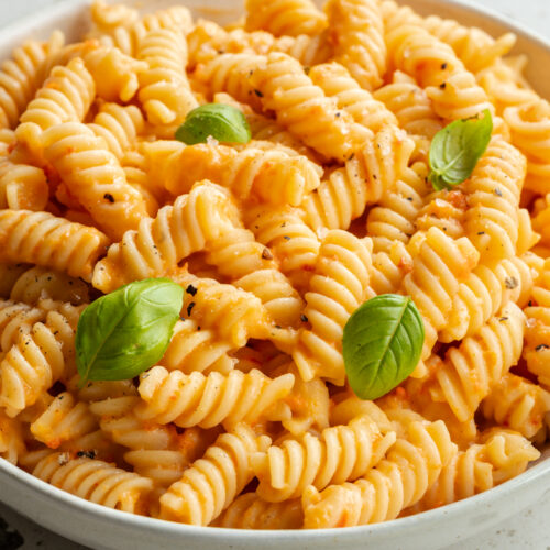 Ein Teller mit Pasta in Paprika Sauce mit weißen Bohnen steht auf dem Tisch.