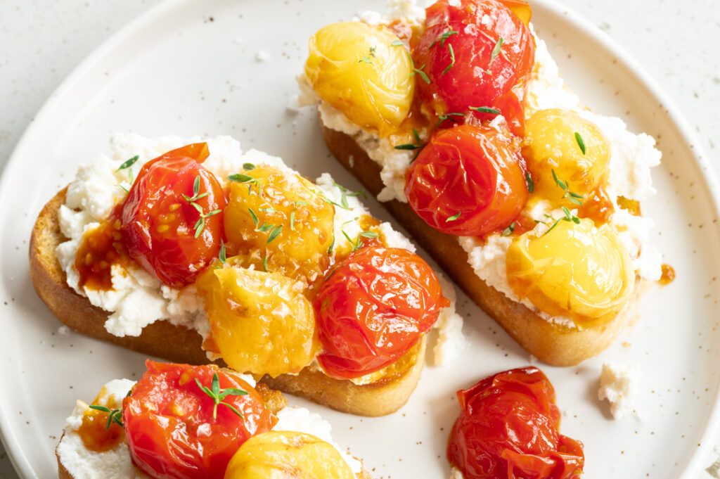 Ein Teller mit geschmorten Tomaten auf Ricotta-Toast steht auf dem Tisch.