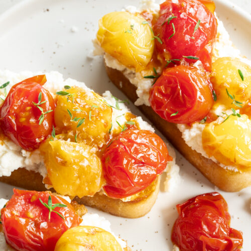 Ein Teller mit geschmorten Tomaten auf Ricotta-Toast steht auf dem Tisch.