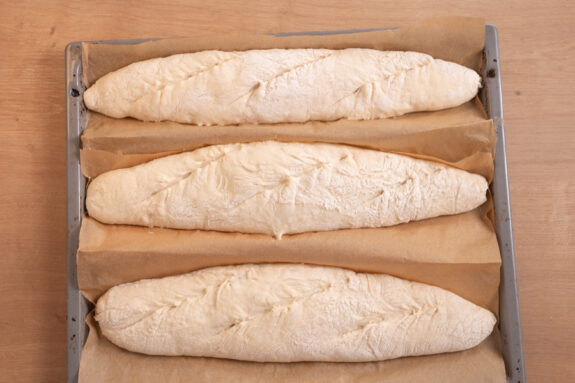 Die Baguettes liegen auf einem Backblech und werden eingeschnitten