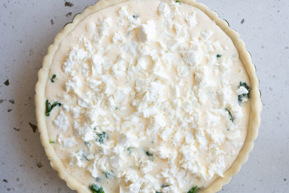 Der Feta wird auf der Quiche verteilt.