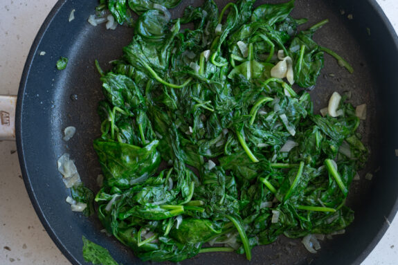 Der Spinat ist zusammen mit der Schalotte und Knoblauch in einer Pfanne.